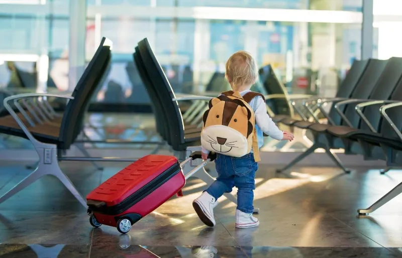 Enfant avec une valise à roulettes et un sac à dos dans un aéroport