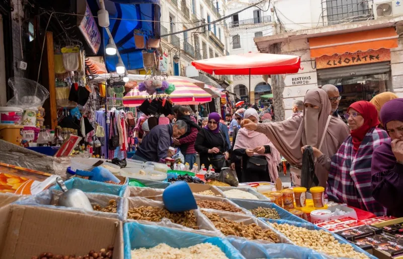 Scène de marchandage dans un marché traditionnel en Algérie avec des étals de fruits secs, d'épices et de produits locaux