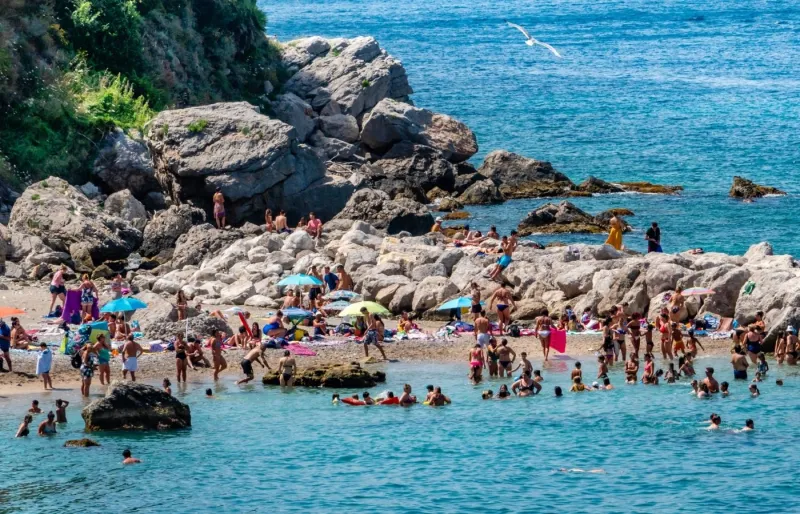 Plage bondée près de Sorrente en été avec des baigneurs profitant de la mer et du littoral rocheux
