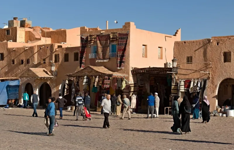 Habitants portant des tenues traditionnelles sur une place du Sahara algérien, illustrant les usages vestimentaires en Algérie